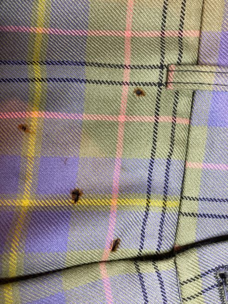 Close-up of holes in tartan fabric on a pair of trousers, showing areas needing mending in Motherwell.