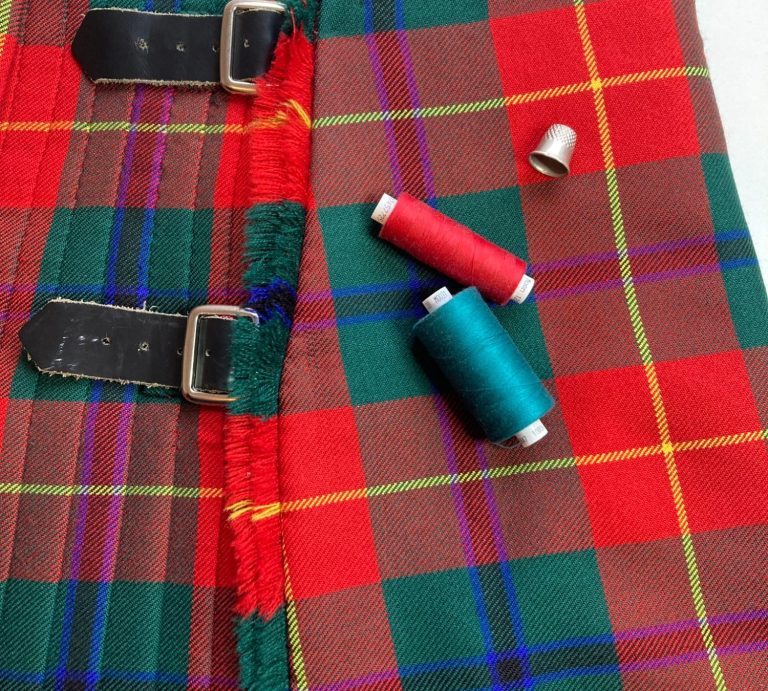 Tartan fabric with sewing threads in red, teal, and a metal thimble.