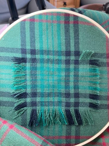 Invisible mending in progress on moth - damaged tartan