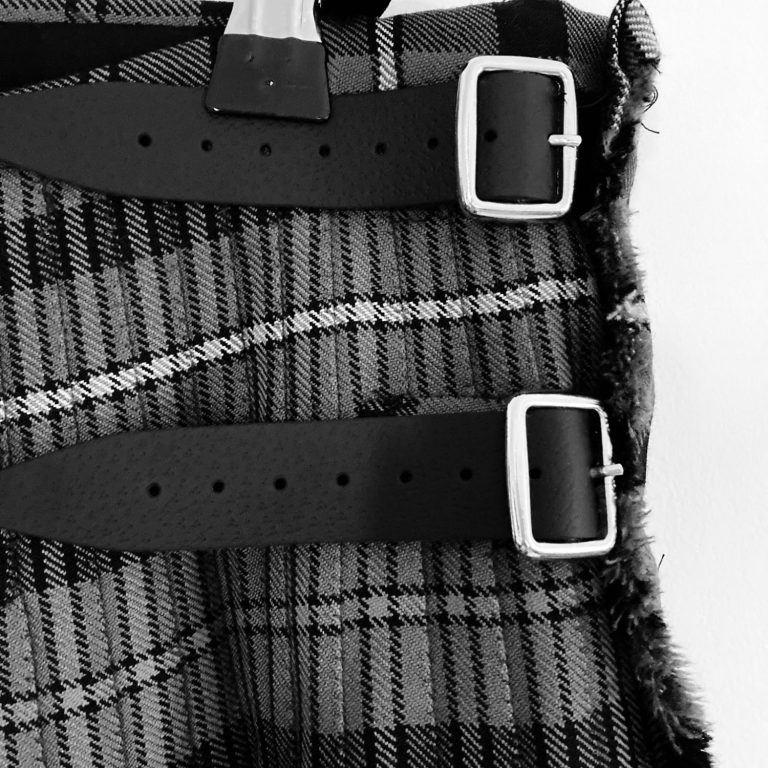 Close-up of a black and grey kilt with two black leather straps and silver buckles.