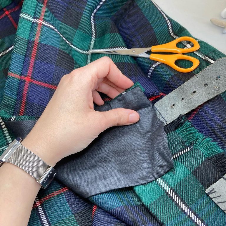 A hand holding a black fabric patch on a tartan fabric, with scissors nearby.